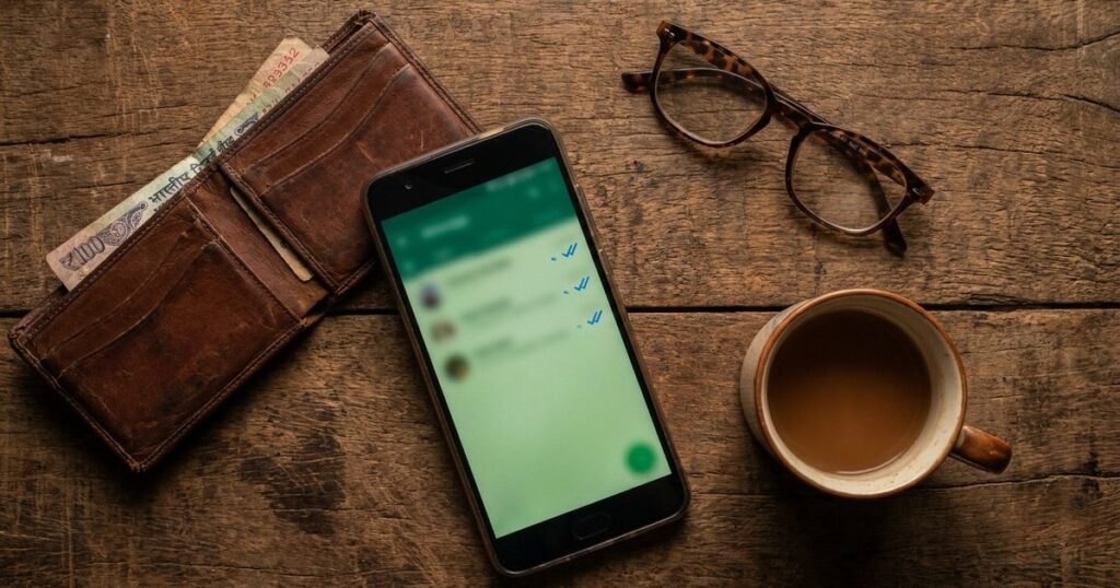 A wooden table with a WhatsApp message, chai, and wallet, illustrating sales conversations transitioning to WhatsApp.