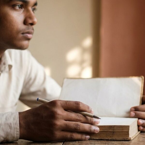 An Indian student pondering career choices as a doctor or IAS officer, seated in a sunlit room with a book and pen.