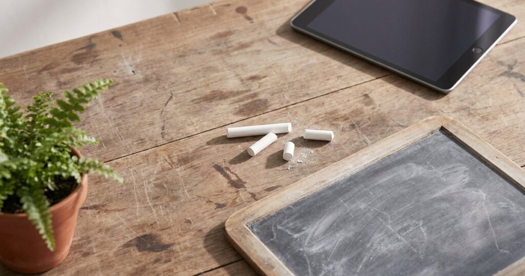 Chalk and a blackboard beside a tablet, illustrating the tension between traditional and AI-driven education methods.