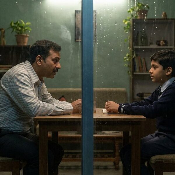 A father and son discuss the worth of Class 6 foundation coaching, seen through a window in an Indian home.