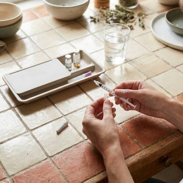 Hands preparing an IVF injection on a warm kitchen table, showing the practical side of fertility treatment
