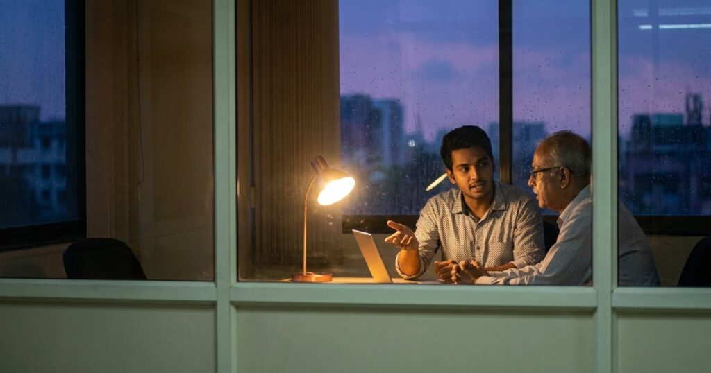 Two people discussing AI startups in India seen through a doorway, reflecting the article's focus on angel investors.